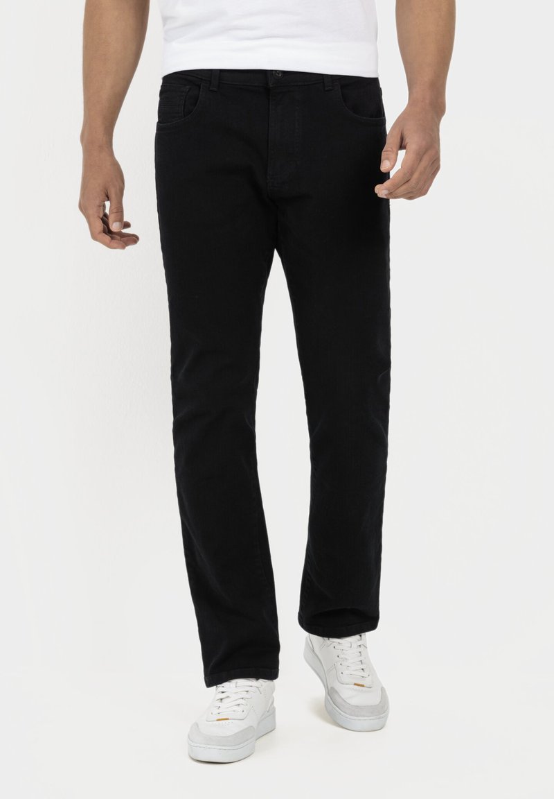 Sorte denim jeans med lige pasform, fem lommer og knaplukning. Stoffet har en glat tekstur. Båret med hvide sneakers.