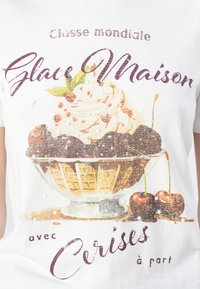 White t-shirt featuring a colorful ice cream sundae illustration, sprinkled with textures, cherries, and stylized text in purple and brown.
