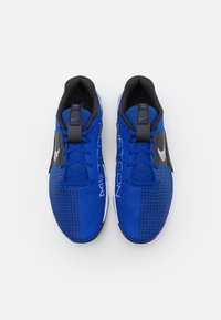 Pár modro-černých atletických bot s mesh texturou, černými poutky na patě a bílým logem ve tvaru šeku, z pohledu shora na bílém pozadí.