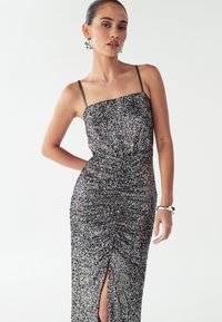 Mustast litritega õhtukleit, millel on ruudukujuline kaelus, õhukesed rihmad ja külje peal lõhik. Kangas on tekstuuriga ja kehapidi, rõhutades siluetti.