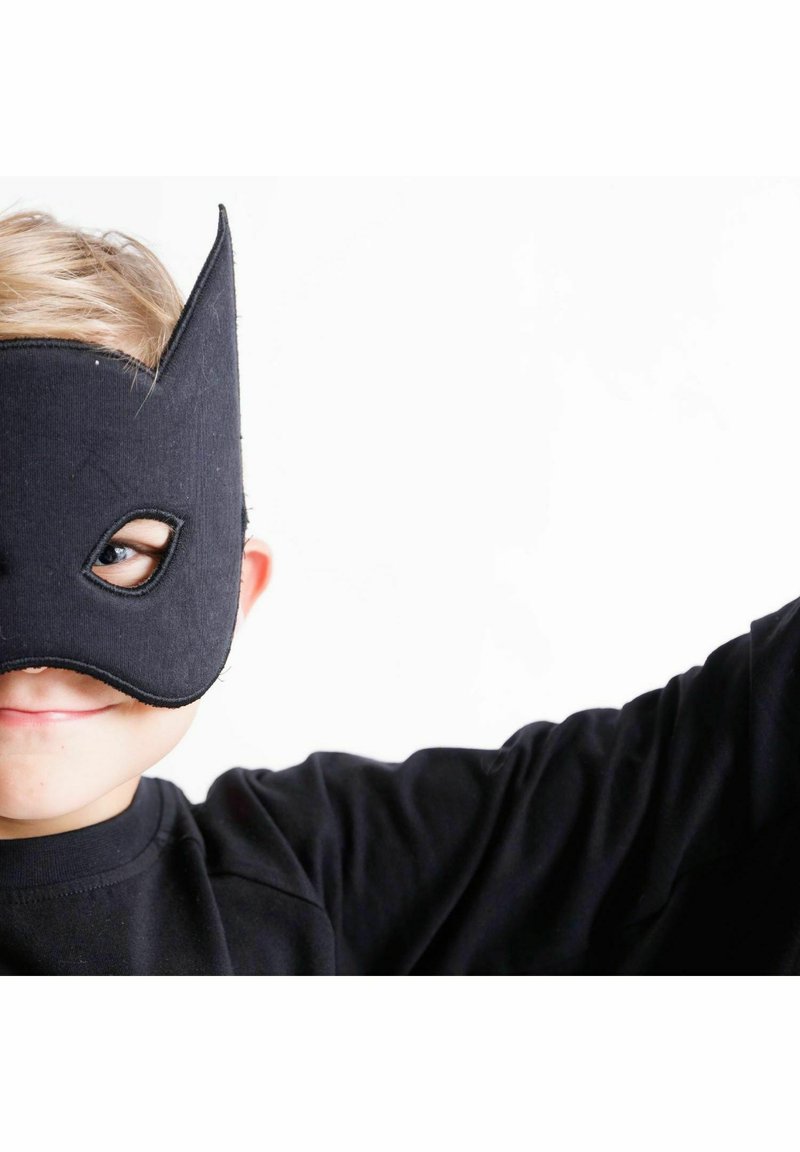 Svart tygmask med spetsiga öron och ögonutskärningar, bärs av ett barn i en svart långärmad tröja mot en vit bakgrund.
