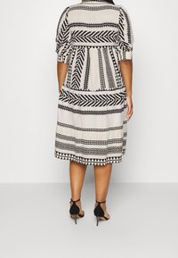 Vestido con estampado en negro y crema, de diseño en capas, con mangas cortas abullonadas y dobladillo acampanado. Llevado con tacones negros con tiras.