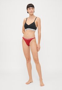 Black bralette with grey logo band and red bikini bottom with matching logo band. Minimalist design with a smooth texture.