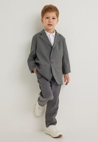 Szary żakiet z dwoma guzikami, w zestawieniu z dopasowanymi szarymi spodniami i białymi trampkami. Żakiet ma kołnierz typu lapel i jest skrojony.