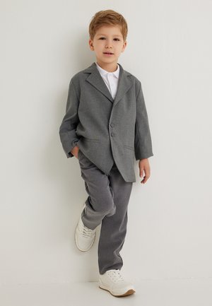 Blazer gris con dos botones, combinado con pantalones grises a juego y zapatillas blancas. El blazer tiene un cuello de solapa y está entallado.