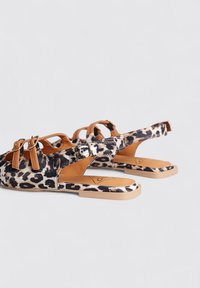 Sandalias de estampado de leopardo con correas de cuero marrón, diseño de punta abierta y hebillas. La suela es plana con una base beige.