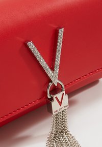 Clutch in pelle rossa con un emblema a forma di 'V' decorato con borchie argentate, una frangia di catena argentata e un lucchetto metallico con il marchio "Valentino".