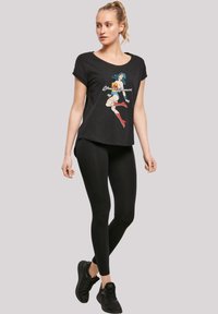 Juodas marškinėliai su spalvinga Wonder Woman grafika, derinami su juodomis legginsais ir juodais sportiniais bateliais. Marškiniai laisvai krenta ir turi trumpas rankoves.