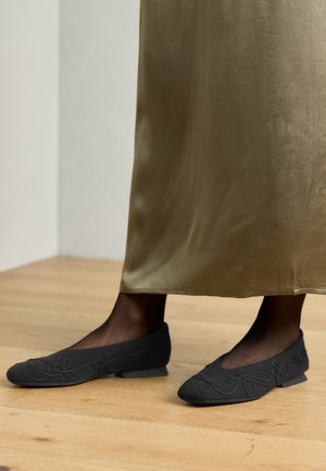 Zwarte platte schoenen met bloemenborduurwerk, lage vierkante hak, ronde teen, gemaakt van zacht materiaal, gecombineerd met een satijnen olijfgroene rok.