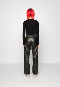 Schwarzes, geripptes Langarmoberteil, kombiniert mit hoch taillierten schwarzen Kunstlederhosen. Die Hosen haben ein weit geschnittenes Design und eine glatte Textur. Silbere Sneakers.