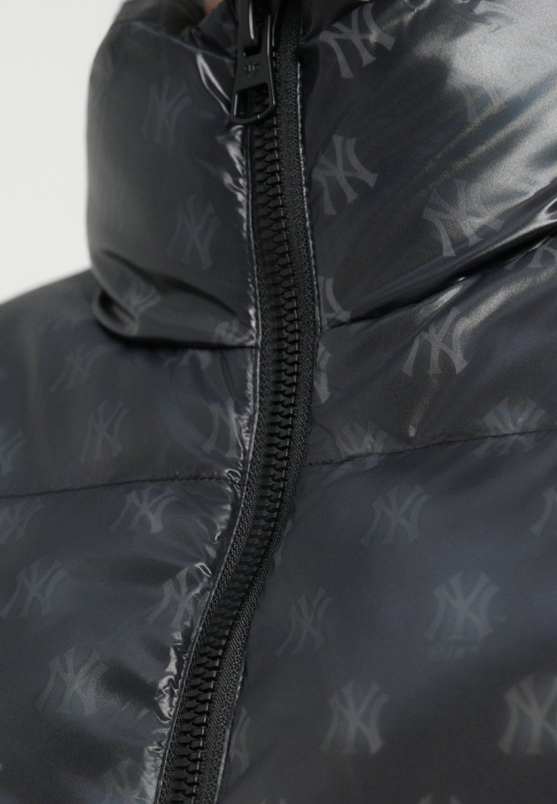 Close-up of black puffer jacket with subtle repeating "NY" logos and a central black zipper.