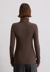 Braunes Langarm-Turtleneck-Top mit taillierter Passform, ausgestattet mit geripptem Textil und hohem Kragen, kombiniert mit grauen Hosen.