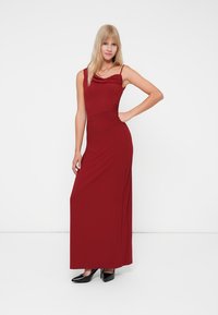 Rochie maxi burgundă cu decolteu drapat, bust ajustat și material neted. Purtați cu pantofi cu toc înalt negri, pe un fundal alb.