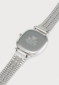 Montre Casio en acier inoxydable argenté avec un boîtier carré, un bracelet en maille métallique et des détails gravés au dos, comportant des informations sur la résistance à l'eau.