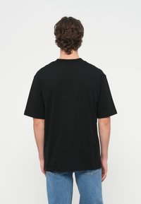 Μαύρο βαμβακερό t-shirt με κοντά μανίκια και στρογγυλή λαιμόκοψη, με άνετη εφαρμογή και λεπτή υφή, εμφανιζόμενο από πίσω.