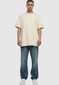 Krem oversized t-skjorte, bomullsstoff, korte ermer, kombinert med lyseblå jeans, rett ben, lett falming, og hvite joggesko.