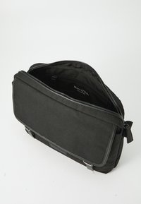 Borsa per laptop nera con chiusura a zip, tessuto liscio e una linguetta anteriore. L'interno presenta una tasca e un'etichetta con il marchio. Cinghie regolabili.