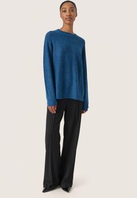 Maglione blu lavorato a maglia con maniche lunghe, scollo rotondo e motivo testurizzato, abbinato a pantaloni neri a vita alta e a gamba larga e scarpe con punta.