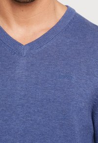 Niebieski bawełniany sweter z dekoltem w serek, posiadający subtelną fakturę oraz logo Esprit w tym samym kolorze po lewej stronie klatki piersiowej.