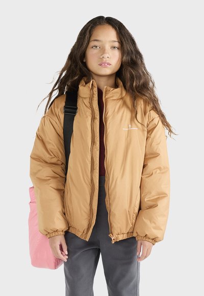 Giacca imbottita color cammello, con colletto alto, polsini elastici e vita elastica. Indossata sopra un top bordeaux con pantaloni grigi; borsa rosa visibile.