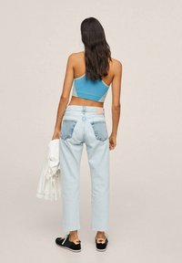 Vaqueros de mezclilla azul claro con piernas rectas, dos bolsillos traseros. Un top corto turquesa y zapatillas negras con cordones blancos y detalles decorativos.