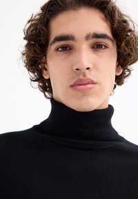 Suéter negro de cuello alto hecho de tejido de punto acanalado, con un diseño ajustado y una textura suave, y con un detalle minimalista.