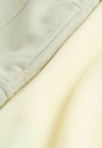 Deux échantillons de tissu : un gris clair, texture douce, et un crème, légèrement nervuré. Détails de couture visibles le long des bords.