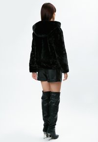 Sort faux fur hoodie jakke med hætte, der har en blød tekstur, parret med sorte læder shorts og knæhøje stiletto støvler.