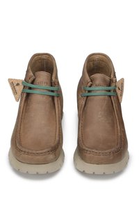 Stivali alla caviglia in pelle marrone con una texture morbida, dettagli in pizzo verde e etichetta in sughero. Presentano una punta arrotondata e una robusta suola beige.