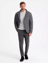 Doudoune gris foncé avec un design à col, des coutures horizontales et des poches avant. Associée à une chemise gris clair et un pantalon foncé.