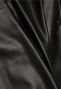 Sileä musta nahkakangas, jossa on näkyvä hienojakoinen rakenne, pehmeästi taitettuna luoden hellävaraisia kaarevia linjoja ja korostuksia.