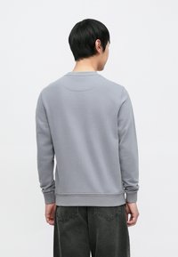 Grå genser med lange ermer, rund hals og ribbestrikkede mansjetter. Mykt stoff med en jevn tekstur; bakfra, kombinert med mørke bukser.