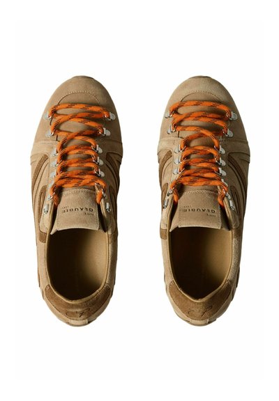 Paire de baskets en suède marron clair avec des lacets à motif orange et noir, des œillets en métal et le nom de la marque embossé sur la languette.