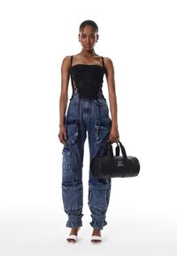 Zwart gebreid korsettopje, lichtblauwe wijde cargobroek met zakken en zwarte leren duffeltas. Model draagt witte sandalen met hak.