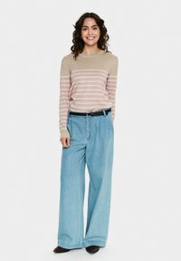 Beige tröja med rosa ränder, kombinerad med ljusblå vida jeans och ett svart bälte. Modellen står framför en neutral bakgrund.