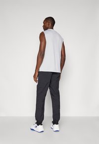 Ærmeløs grå top, sorte teksturerede bukser med elastiske manchetter og hvide sneakers med blå accenter. Rene linjer, afslappet pasform, enkelt design.