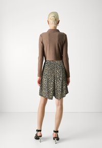 Smeđa rebrasta majica dugih rukava u kombinaciji s suknjom u leopard uzorku, koja ima elastičan pojas. Crne sandale s petom s ukrasnim detaljima.
