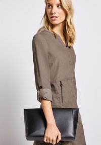 Schwarze Leder-Clutch mit strukturiertem Design, rechteckiger Form und glatter Oberfläche, die in einer Hand vor einem hellen Hintergrund gehalten wird.
