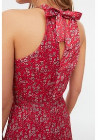 Vestido rojo floral con un corte en la espalda en forma de ojal y un lazo en el cuello, hecho de un tejido ligero y con pequeños patrones florales blancos.