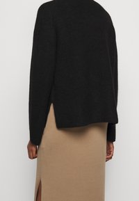 Maglione nero a maglia con una vestibilità ampia, presenta spacchi laterali; abbinato a una gonna lunga beige che mostra uno spacco alto coscia.