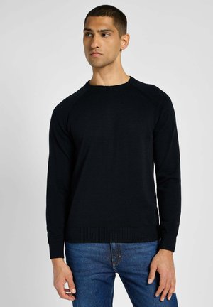 Maglione nero a maglia con maniche lunghe, colletto e polsini a costine. Abbinato a jeans blu, con una vestibilità classica e linee pulite.