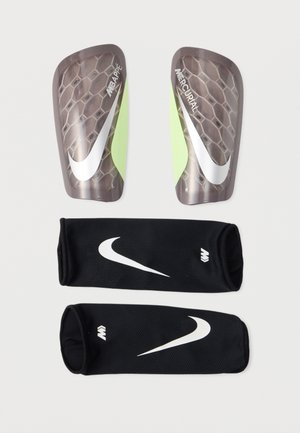 Chrániče holení Nike Mercurial s čiernymi sieťovanými návlekmi, ozdobené bielymi logami Swoosh a značkou Mbappé, zobrazené na bielom pozadí.