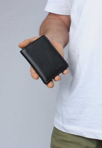 Black leather wallet held in a hand, featuring a simple design with smooth texture and rounded corners, displaying a subtle logo.