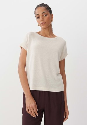 Knit beige short-sleeve top with a wide neckline, relaxed fit, and subtle texture. Paired with dark brown pants.