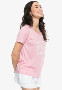 Lichtroze t-shirt met korte mouwen met een witte afbeelding van palmbomen en de tekst "SUNSET ESCAPE." Zachte stof met een relaxte pasvorm.