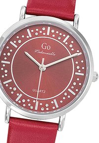 Montre avec bracelet en cuir rouge, boîtier en argent, cadran rond, mouvement à quartz, et index heures en strass sur un fond texturé rouge.