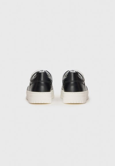 Svarta lädersneakers med en vit gummisul, lätt textur, slät yta och rund tå; har en minimalistisk bakdesign.