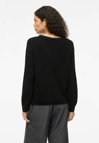 Maglione nero a maglia con texture a coste, maniche larghe e vestibilità rilassata. Visuale posteriore, con dettagli sul collo e sull'orlo.