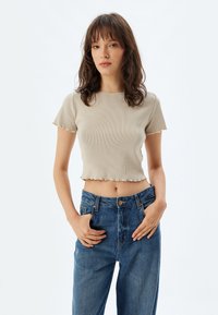 Beige ribbad croptop med vågig kant och korta ärmar, matchad med högmidjade blå denimjeans. Enkelt, figurnära design.