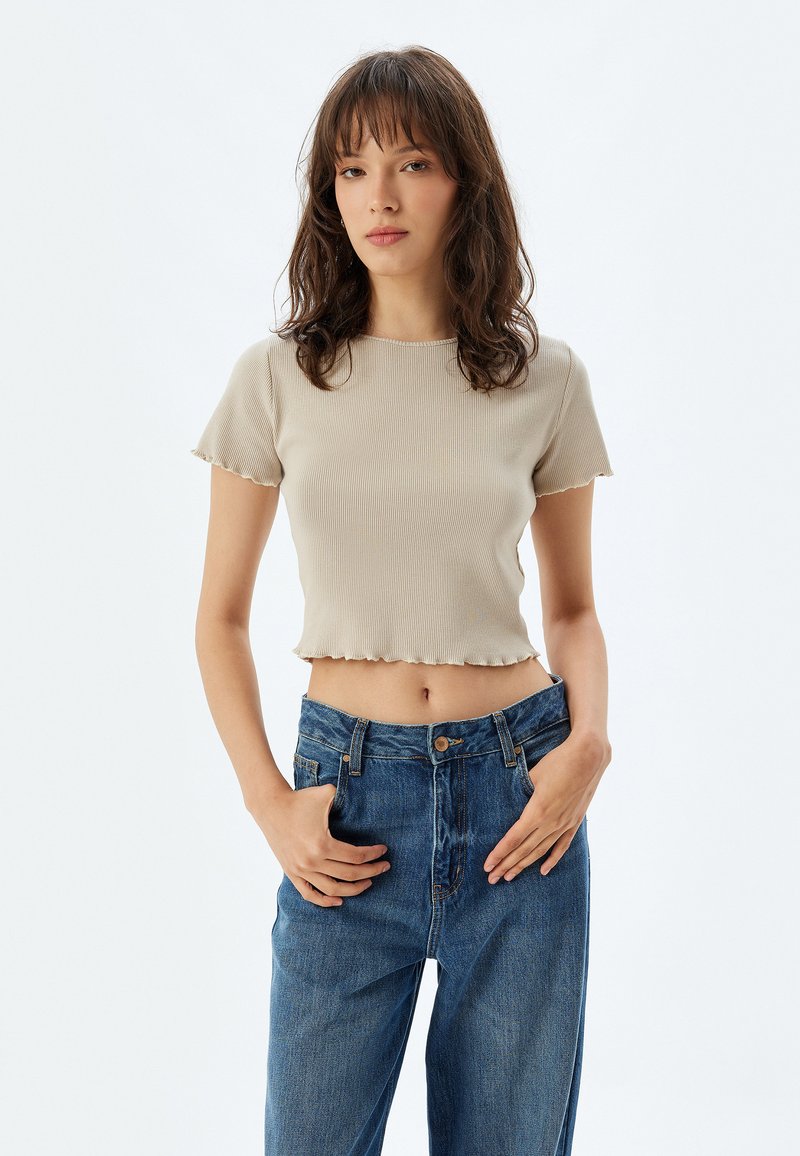 Beige ribbad croptop med vågig kant och korta ärmar, matchad med högmidjade blå denimjeans. Enkelt, figurnära design.